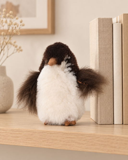 Peluche pingouin en laine d’alpaga de 15 cm sur une étagère, à côté de livres